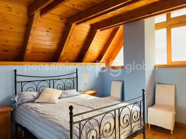 Dormitorio con cama de matrimonio, techo panelado y pared abuhardillada.