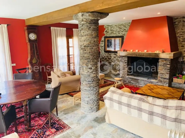 Salón con sofá y sillón, pequeña mesa de comedor y una gran chimenea abierta.