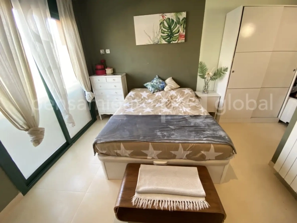 Amplio dormitorio con cama doble con ventanales del suelo al techo.