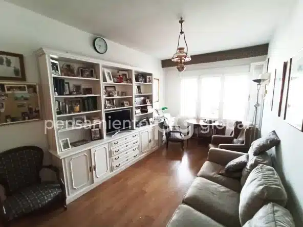 Salón con sofá, sillón y mesa pequeña junto a la ventana.