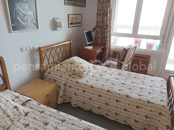 Habitación con dos camas individuales, rincón de trabajo con ordenador y silla y mesita de noche entre las camas.