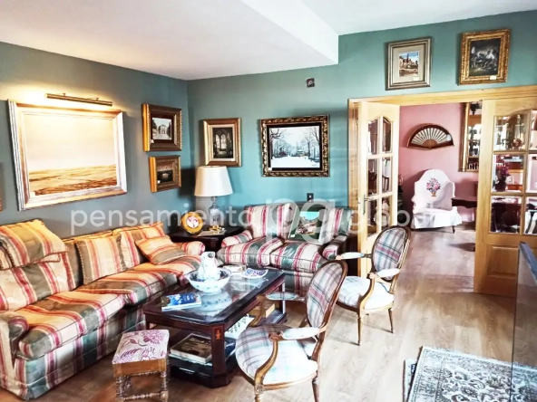 Salón con dos sofás sillas y mesita. Puerta con ventanas abiertas a otro espacio habitable.