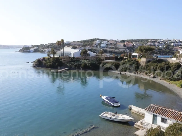 Vista del puerto con dos pequeñas embarcaciones y un cobertizo para botes en primer plano.