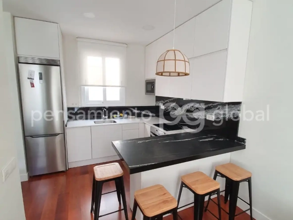 Cocina blanca, nevera de acero inoxidable, ventana sobre el fregadero, cuatro taburetes alrededor de una encimera-espacio para comer