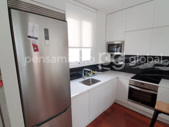 cocina con nevera de acero inoxidable, armarios blancos, ventana